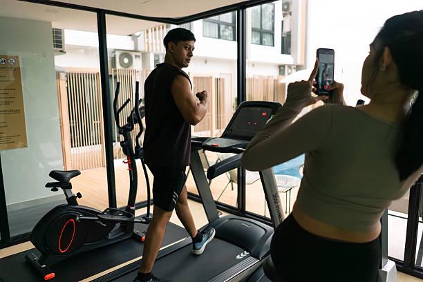 istock Man posing for camera while working out, woman filming him in a modern gym 2253467475