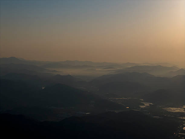 Captivating aerial view of a sunset casting warm hues over a mountain range, with misty valleys below. The scene is tranquil and picturesque, ideal for nature photography or travel promotions.