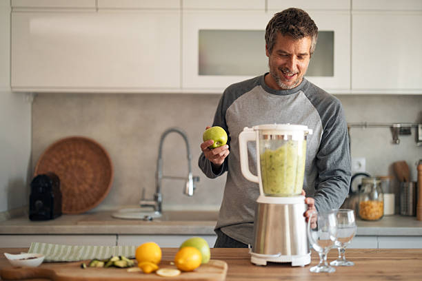 istock Smiling Man Makes Green Smoothie in Modern Kitchen With Blender and Fresh Fruit 2253470018