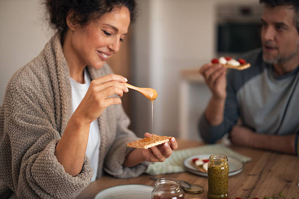 istock Cozy Morning Snack: Woman Spreads Peanut Butter On Crackers While Friend Smiles In Kitchen 2253470848