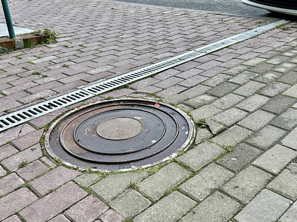 istock Drain Cover Inspection, Paved Surface With Utility Cover, Manhole And Drainage System With Moss And Brick Border, Inspection Scene Of City Utility Access Point With Moss And Brick Edging 2253473916