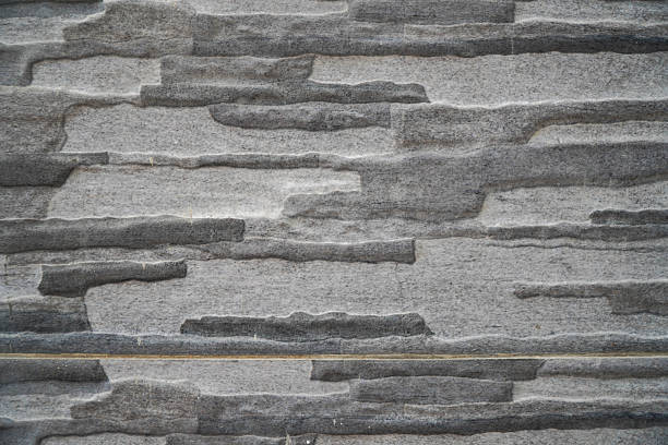 Textured grey wall design showcasing irregularly stacked stone tiles with a distinct horizontal joint Perfect for contemporary architectural backgrounds
