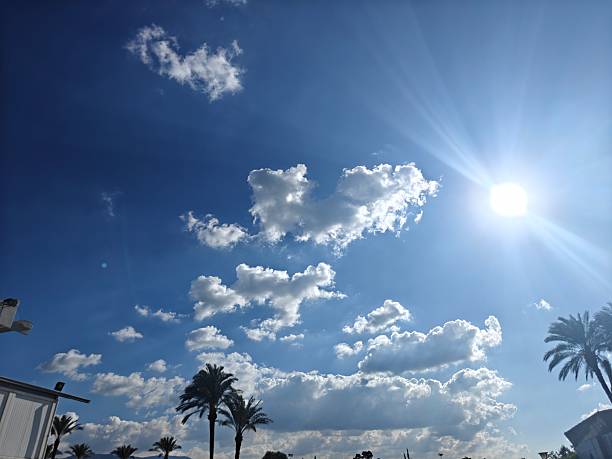 Bright blue sky with scattered white clouds and sunlight rays. Natural sky background with open space, suitable for design, advertising, and outdoor concepts.