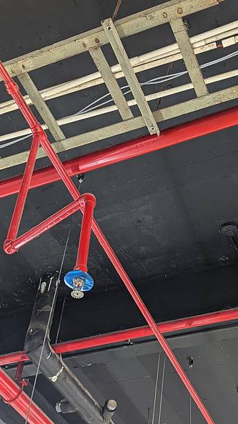 istock Industrial ceiling infrastructure featuring red fire sprinkler pipes, metal cable trays, and exposed wiring, viewed from below, creating a strong geometric pattern and utilitarian atmosphere. 2253477054
