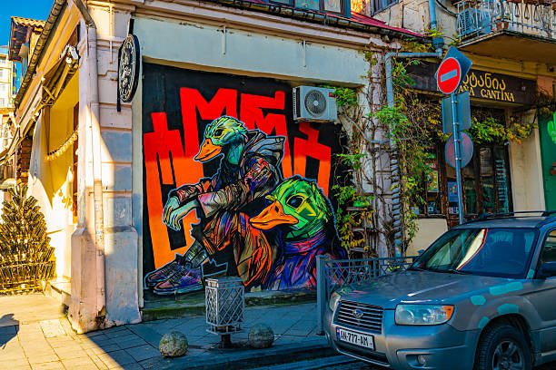 Batumi, Georgia. 02 January 2025  Vibrant street art of two anthropomorphic ducks in neon colors covers the wall of a café in the Old Town, adding a bold splash of urban creativity to the cobbled street lined with parked cars and balconies.