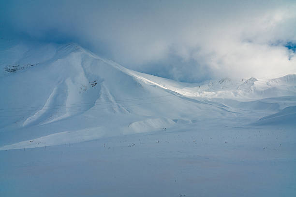 Soft light breaks through clouds over pristine snowcovered peaks near Gudauri ski resort on the Georgian Military Highway, creating a serene winter landscape between Jhinvali Reservoir and the high Caucasus.