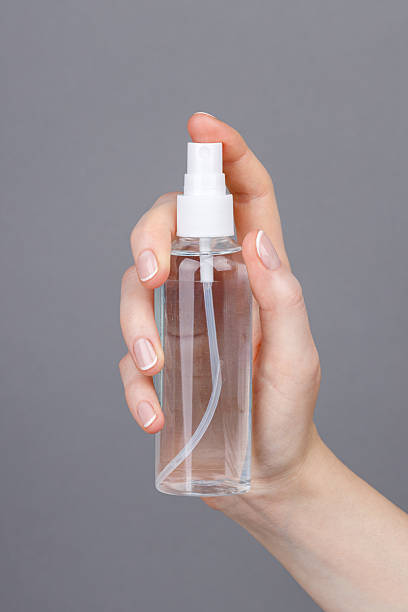 istock Hand holding transparent spray bottle on gray background, Close-up. 2253478137