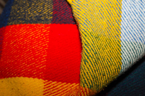A textured wool blanket with a rich checkered pattern combines vibrant red, yellow, and blue colors. This detailed macro shot focuses on the soft pile and dense diagonal weaving of the threads, creating a sense of comfort and warmth.