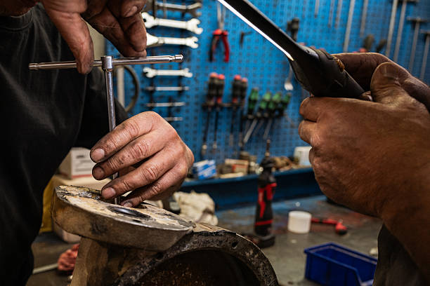 Close-up of a mechanic’s hands using a caliper and hand tools to measure and repair a metal mechanical component inside a workshop. The image highlights precision, craftsmanship, and manual labor in an industrial maintenance environment, with tools and equipment visible in the background.