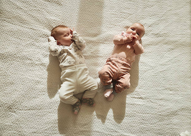 A touching close-up of twin baby girls resting side by side, wrapped in soft white swaddles. Their serene expressions highlight the beauty of new life and the precious bond of sisterhood. Perfectly capturing the tender innocence of their first days in the world