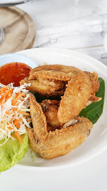 Thai herb fried chicken wings served on a plate at a modern cafe. Crispy golden fried chicken with Thai herbs, popular Thai food menu, casual dining, cafe food lifestyle, and delicious street food style presentation.