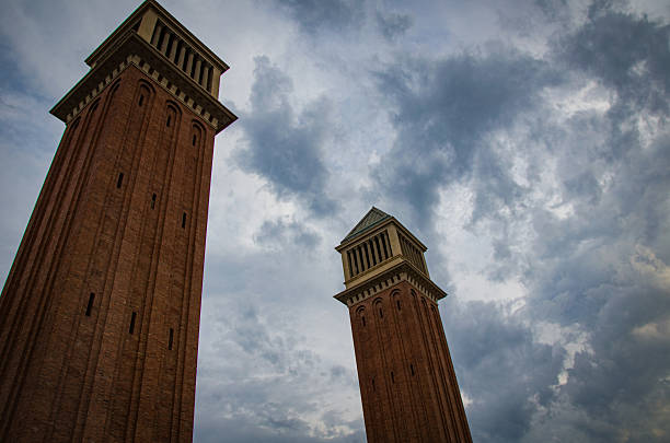 Low angle view of two tall brick towers with rectangular windows against a dramatic cloudy sky background.