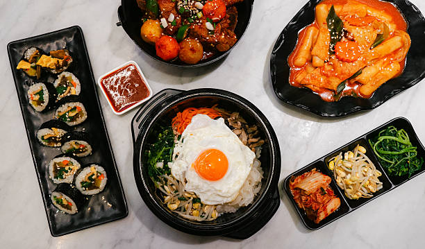 Traditional Korean food set served on a dining table, featuring bibimbap with fried egg, spicy tteokbokki, gimbap and assorted Korean side dishes.
