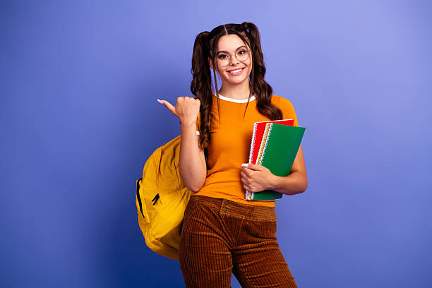 istock Young student girl with backpack and notebooks smiles against purple background 2253487977