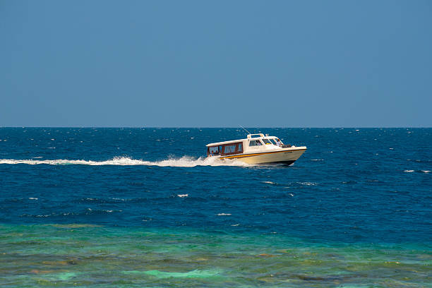 The vibrant turquoise water of the shallow lagoon blends seamlessly into the crystal-clear water of the deep Indian Ocean. An idyllic view of a remote tropical island in the Maldives, featuring lush green palm trees fringed by pristine white sands.