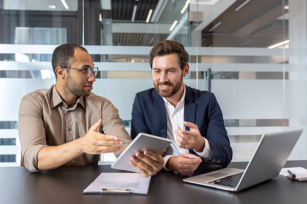 istock Business partners in a modern office collaborate over a tablet and laptop, discussing strategy. 2253495991