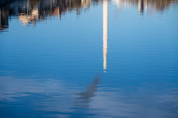 A smoking industrial chimney is reflected in the water's surface.