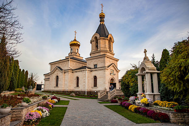 Curchi Monastery complex and beautiful gardens, featuring an Orthodox church with golden domes against a partly cloudy sky, attracting tourists to religious landmarks in Moldova