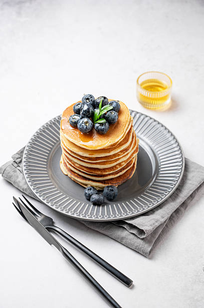istock Stack of pancakes with blueberries and suryp on a gray plate on a light  background 2253504085