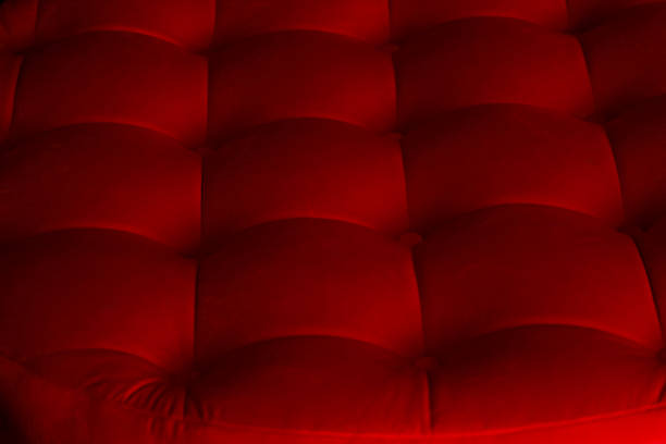 The scene shows a close up view of a red fabric surface. The texture is soft with a grid pattern of raised squares. The lighting highlights the depth and softness of the fabric.
