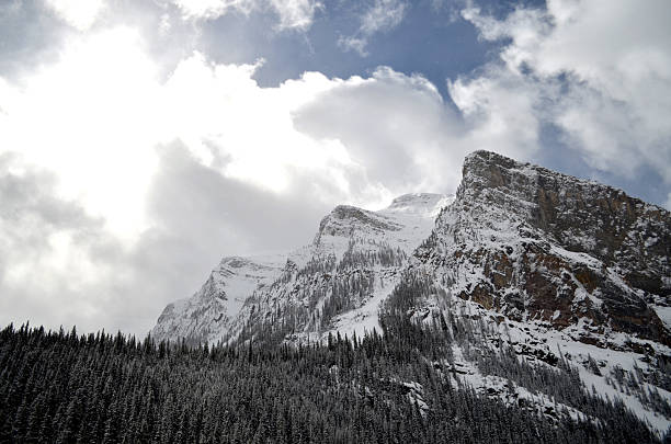 Snow capped rocky mountains peaking out of the clouds above Lake Louise, AB.
