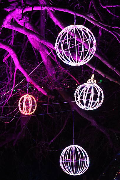 istock Christmas lights at night - large round multi coloured baubles hanging from a tree in a park 2253506380