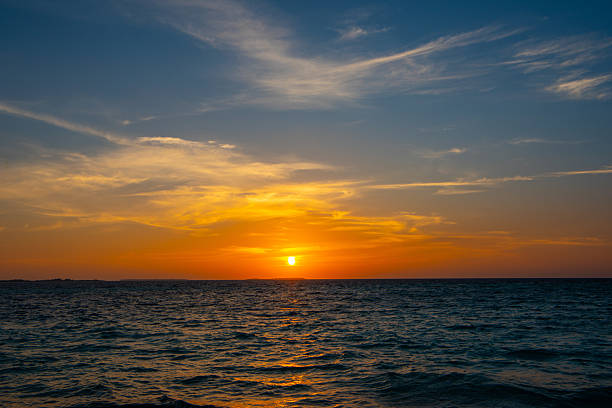 Amazing Maldivian Sunset. The vibrant turquoise water of the shallow lagoon blends seamlessly into the crystal-clear water of the deep Indian Ocean. An idyllic view of a remote tropical island in the Maldives, featuring lush green palm trees fringed by pristine white sands.