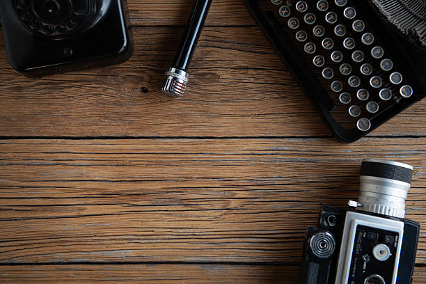 Top view flat lay of a vintage creative workspace with retro typewriter, analog camera, old telephone, classic microphone, magnifying glass and blank instant photo frames on rustic wooden table. Nostalgic background with copy space for text, design, storytelling, journalism and creative concepts.