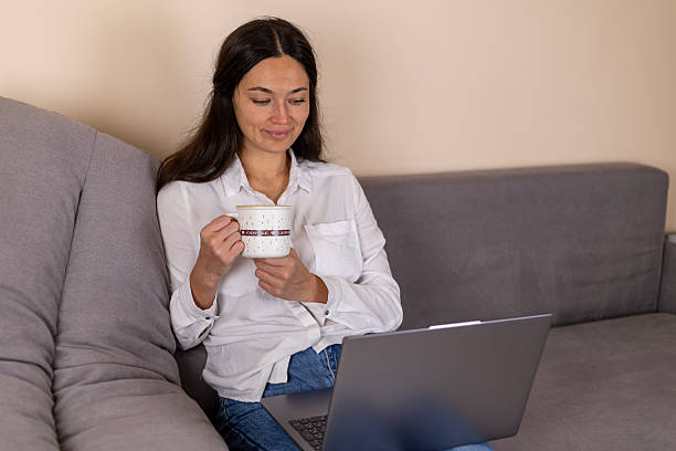 istock Woman working on laptop while relaxing with coffee on a sofa 2253507702