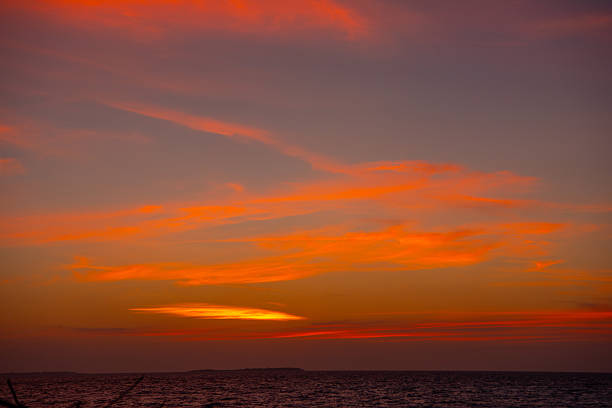 Amazing Maldivian Sunset. The vibrant turquoise water of the shallow lagoon blends seamlessly into the crystal-clear water of the deep Indian Ocean. An idyllic view of a remote tropical island in the Maldives, featuring lush green palm trees fringed by pristine white sands.