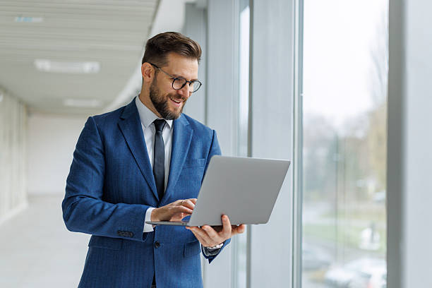 istock Confident businessman working on laptop in modern office hallway 2253513653