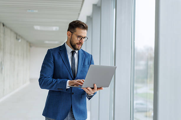 istock Modern businessman typing on laptop standing in office hallway 2253513759