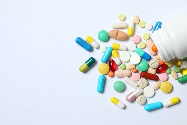 istock Various pills pouring out of a medicine bottle on white background 2253521189