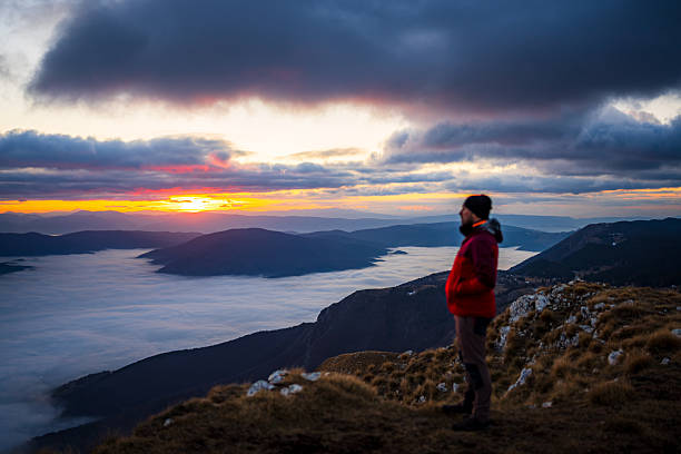 istock Hiker Walking Along Mountain Edge at Sunset with Clouds Rolling Through Valleys 2253522013