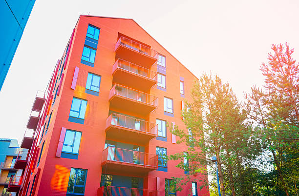 istock Red facade building surrounded by pine trees. Vibrant red apartment complex stands tall with balconies in sunlight. 2253524249