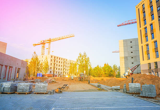Paving bricks at construction site. Laying paving slabs. Ground Compactor Plate on compact soil. Vibratory plate on compacting beating sand for sidewalk. Tower crane on building construction.