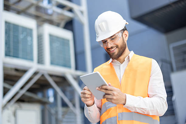 istock A cheerful engineer, in protective gear, uses a tablet while inspecting machinery outside. 2253525524