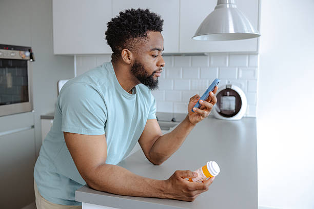 istock Young man in a modern kitchen examines medicine bottle while using his phone 2253525775