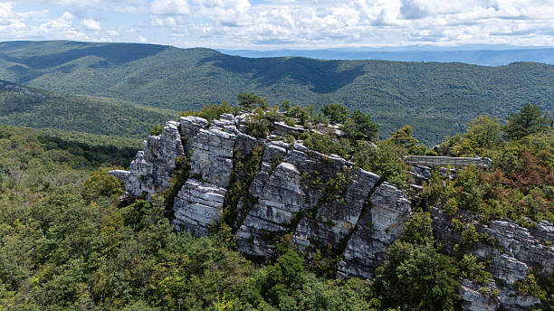 Aerial view of jagged limestone rock formations at the peak of Big Schloss in George Washington National Forest, overlooking a vast valley and rolling Appalachian mountains under a cloudy sky.