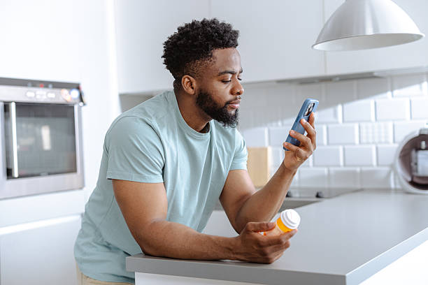 istock Young man in a bright modern kitchen takes medication while checking his phone amid a daily routine 2253525877