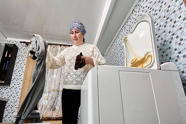 Extraction of washed laundry from automatic top loading washing machine, woman in her 50s prepares to take laundry for drying.