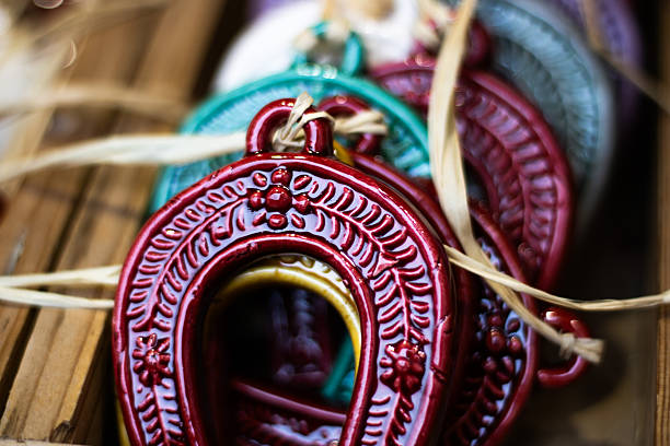 A collection of brightly colored ceramic horseshoe-shaped decorations displayed in a wooden crate. The handmade pieces feature detailed floral engravings and glossy finishes in red, green, and purple hues.