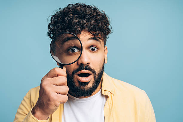 istock Shocked man discovering something surprising using magnifying glass isolated on blue background 2253531138