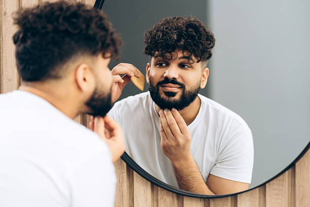 istock Young handsome man grooming beard in bathroom mirror at home 2253531156