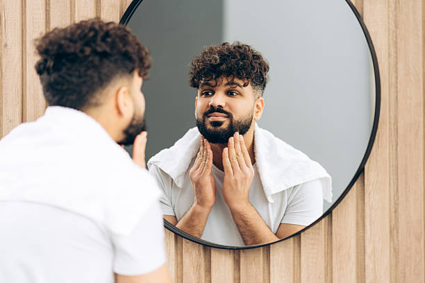 istock Bearded man applying aftershave, practicing daily beard grooming routine looking in mirror 2253531158