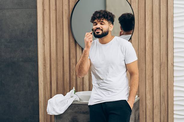 Smiling handsome middle eastern man enjoying self-care grooming routine with jade roller. Skin care concept