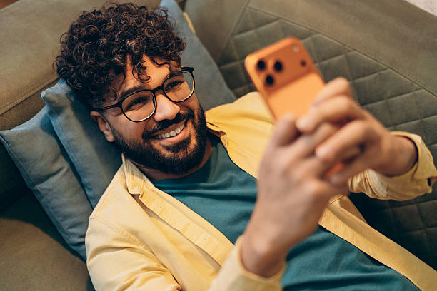 istock Happy smiling middle eastern man in eyeglasses relaxing on sofa using mobile phone 2253531181