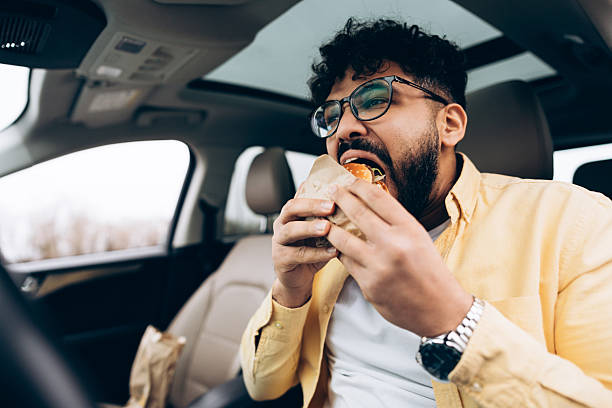 istock Young handsome man eating burger in car from drive-thru 2253531199