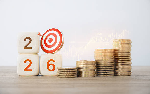 istock 2026 Written Wood Blocks and Red Bull's Eye Target on Coin Stacks with Financial Chart Before Defocused Background. 2253534708