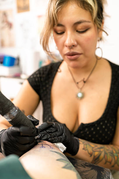 istock Female tattoo artist working on client arm in studio 2253538574